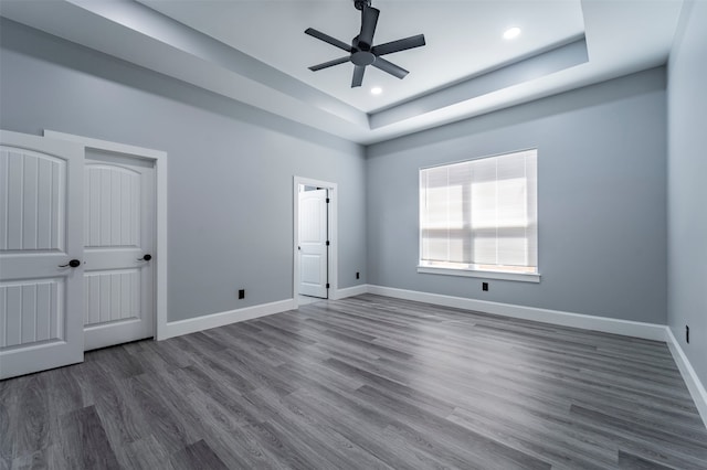 unfurnished bedroom with ceiling fan, a raised ceiling, and dark hardwood / wood-style flooring