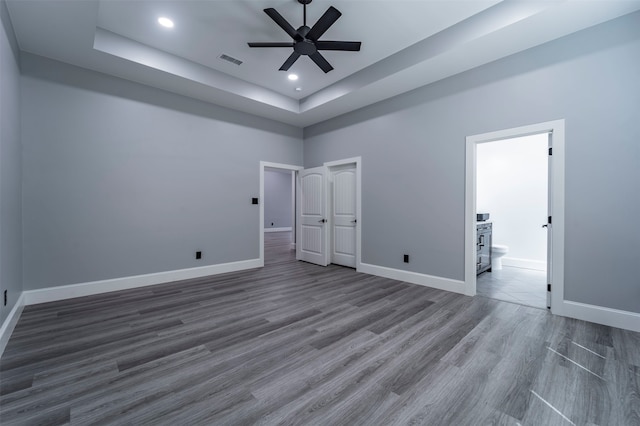 unfurnished bedroom with ceiling fan, a raised ceiling, dark hardwood / wood-style flooring, and ensuite bath