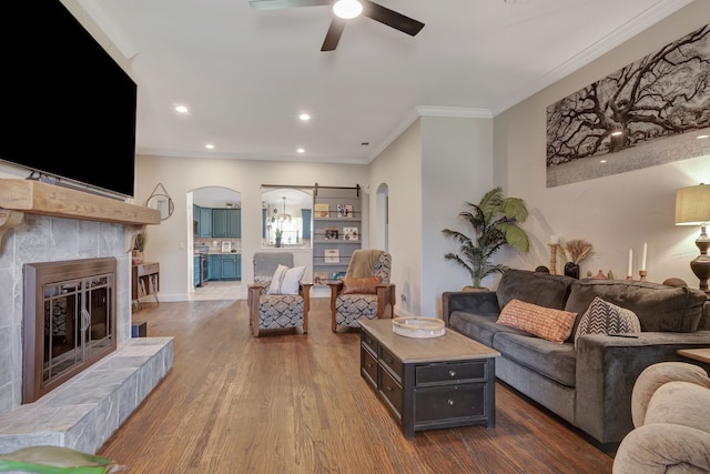 living room with crown molding, a fireplace, ceiling fan, and wood-type flooring