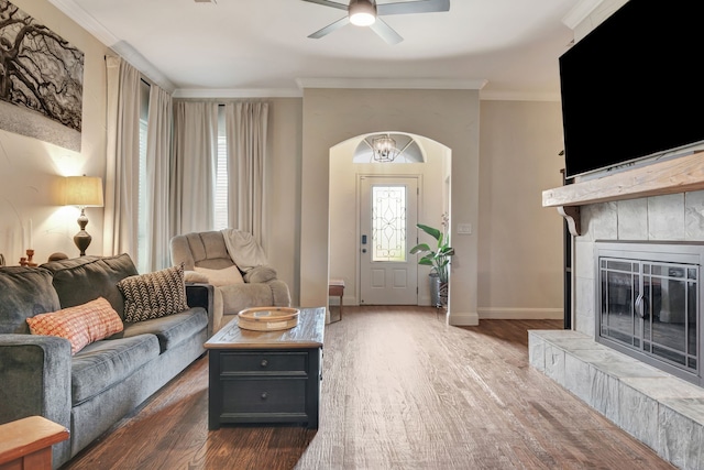 living room featuring a tile fireplace, crown molding, dark hardwood / wood-style flooring, and ceiling fan with notable chandelier