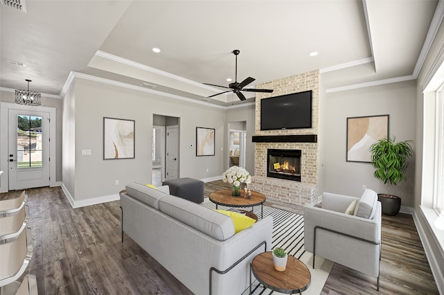 living room with a fireplace, dark hardwood / wood-style flooring, a tray ceiling, and ceiling fan with notable chandelier