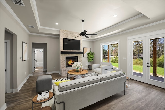 living room with ceiling fan, a raised ceiling, dark hardwood / wood-style flooring, crown molding, and a fireplace