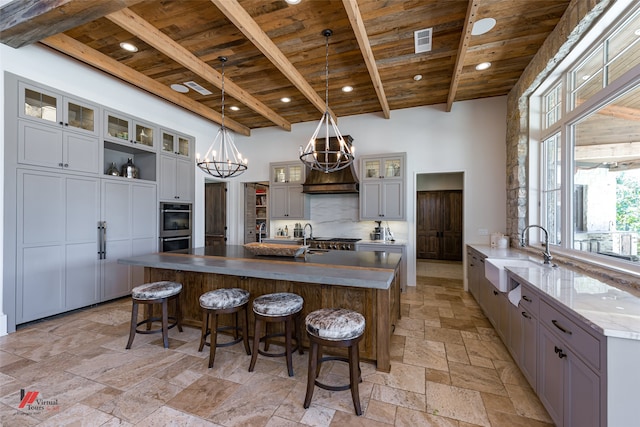 kitchen with sink, light tile patterned flooring, pendant lighting, and a center island with sink