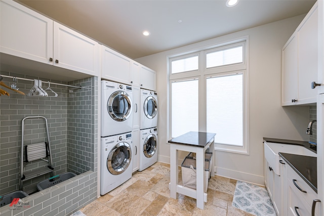 laundry room featuring light tile patterned floors, stacked washing maching and dryer, cabinets, and plenty of natural light