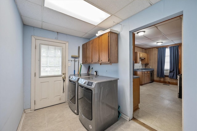 laundry room featuring cabinets, sink, wooden walls, light tile patterned floors, and washing machine and clothes dryer