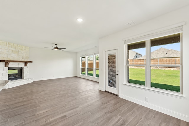 unfurnished living room featuring a wealth of natural light, ceiling fan, hardwood / wood-style flooring, and a stone fireplace