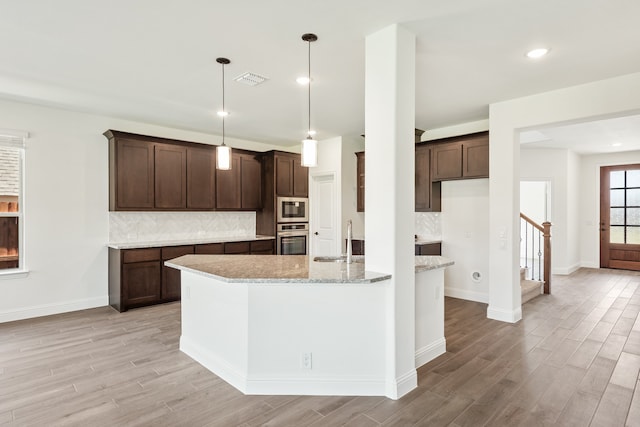 kitchen featuring light hardwood / wood-style floors, light stone counters, pendant lighting, stainless steel appliances, and sink