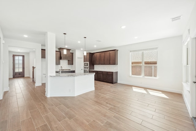 kitchen featuring appliances with stainless steel finishes, light hardwood / wood-style flooring, light stone counters, and decorative light fixtures