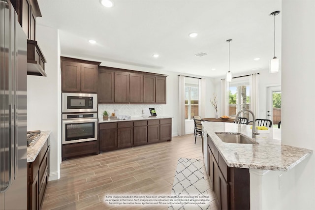 kitchen featuring light stone counters, pendant lighting, stainless steel appliances, light wood-type flooring, and sink