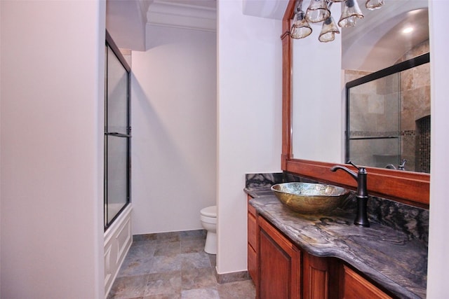 bathroom featuring vanity, baseboards, stone finish floor, toilet, and combined bath / shower with glass door