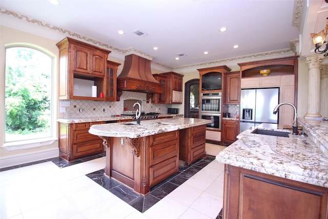 kitchen with visible vents, custom exhaust hood, an island with sink, a sink, and appliances with stainless steel finishes