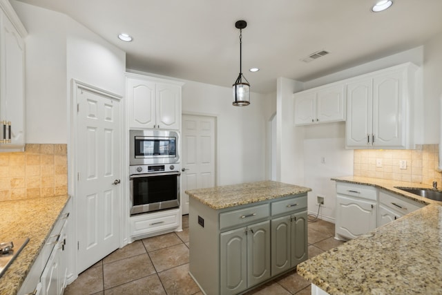 kitchen with a kitchen island, light stone countertops, pendant lighting, and white cabinetry