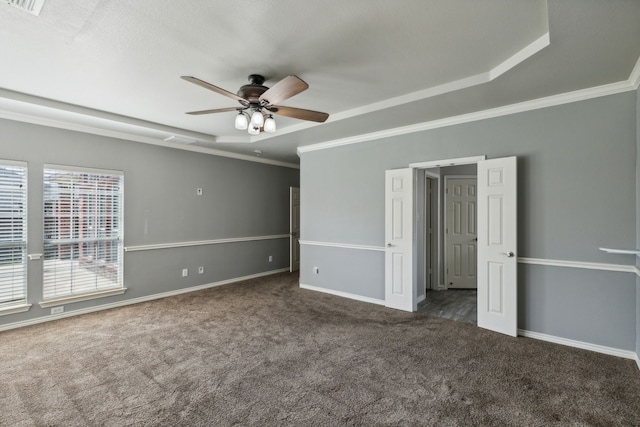 unfurnished bedroom featuring ornamental molding, ceiling fan, a tray ceiling, and dark carpet