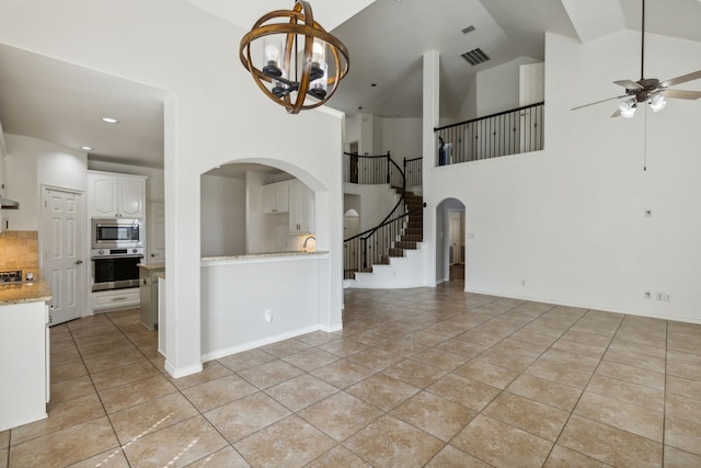 interior space featuring light tile patterned flooring, high vaulted ceiling, and ceiling fan with notable chandelier