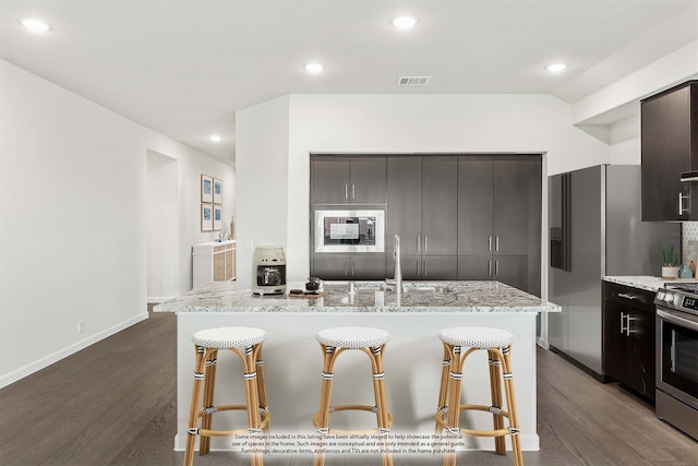 kitchen with an island with sink, appliances with stainless steel finishes, dark hardwood / wood-style flooring, and a kitchen breakfast bar