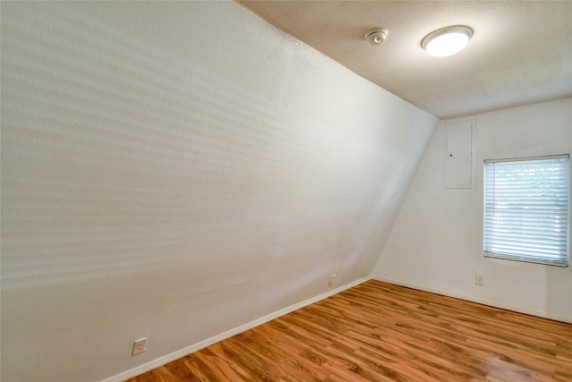 empty room featuring a textured ceiling, electric panel, wood-type flooring, and vaulted ceiling