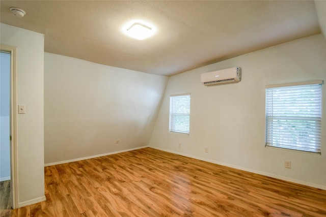 unfurnished room with a wall mounted air conditioner, lofted ceiling, and light hardwood / wood-style flooring