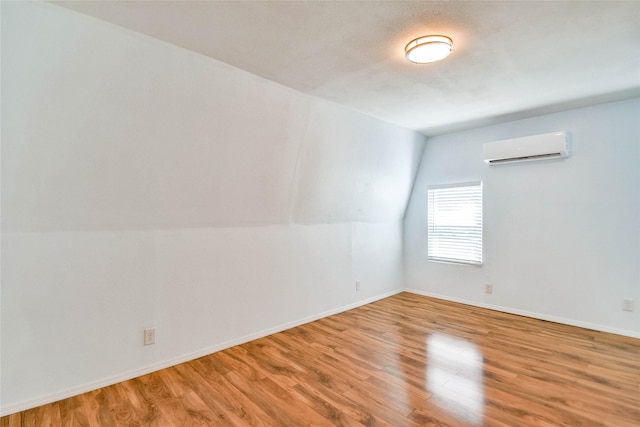 empty room featuring lofted ceiling, hardwood / wood-style floors, and a wall mounted air conditioner