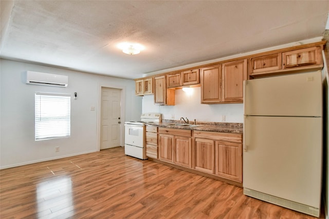 kitchen with sink, a wall mounted AC, dark stone counters, white appliances, and light wood-type flooring