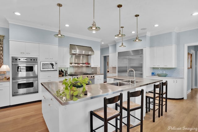 kitchen featuring tasteful backsplash, a kitchen island with sink, built in appliances, wall chimney exhaust hood, and light wood-type flooring