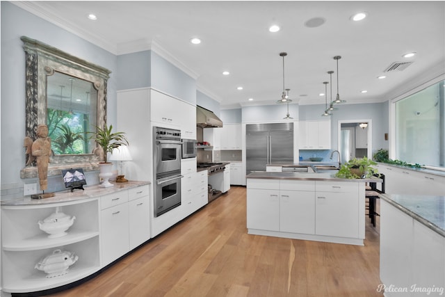 kitchen featuring white cabinetry, a center island with sink, light hardwood / wood-style flooring, stainless steel appliances, and backsplash