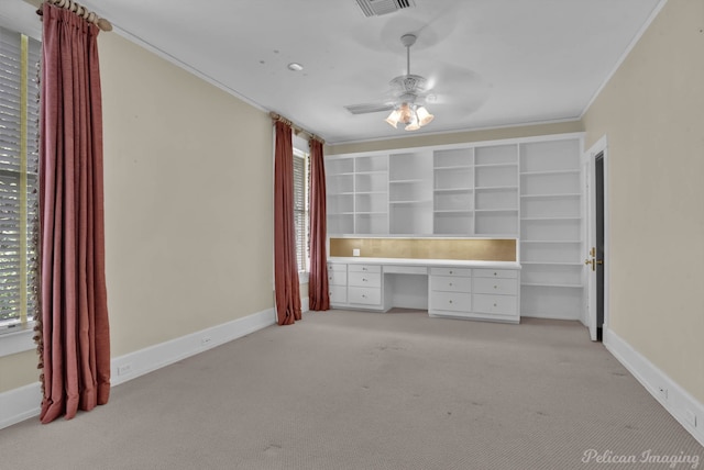 unfurnished bedroom featuring built in desk, ornamental molding, carpet flooring, and ceiling fan