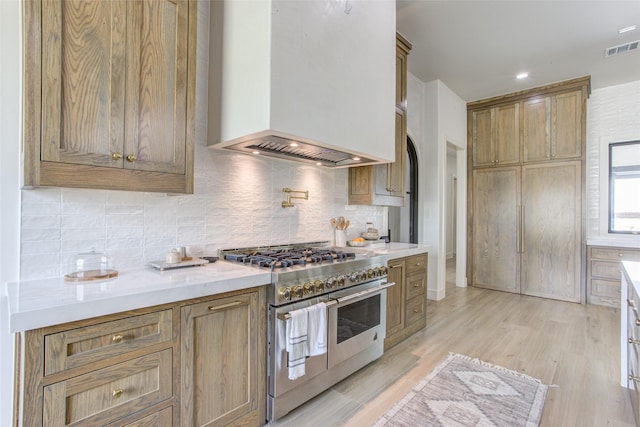 kitchen with backsplash, double oven range, premium range hood, and light wood-type flooring