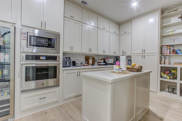 kitchen with backsplash, light hardwood / wood-style flooring, appliances with stainless steel finishes, a kitchen island, and white cabinetry