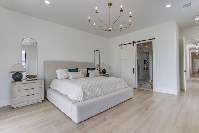 bedroom featuring connected bathroom, a barn door, light hardwood / wood-style flooring, and a chandelier