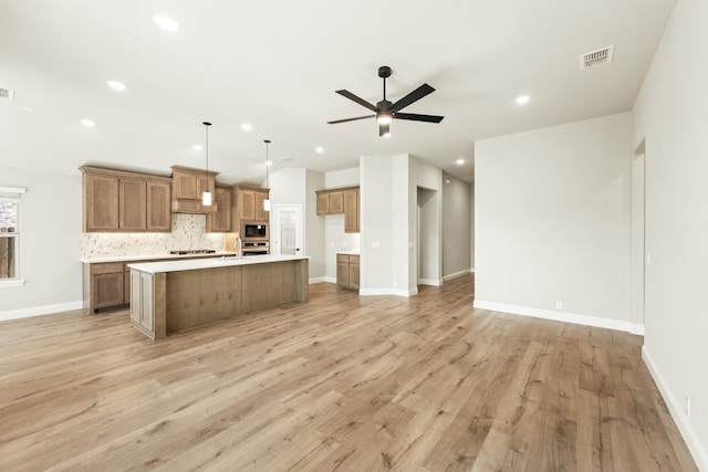 kitchen featuring stainless steel microwave, light wood-type flooring, an island with sink, and hanging light fixtures