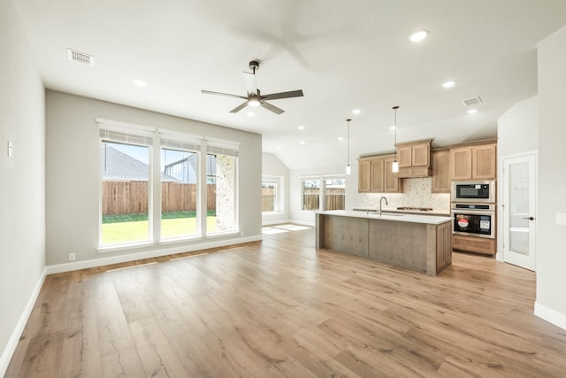 kitchen featuring stainless steel microwave, light hardwood / wood-style floors, lofted ceiling, pendant lighting, and a center island with sink