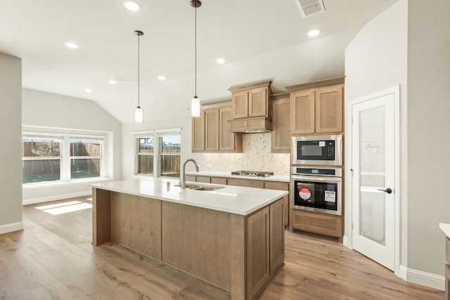 kitchen with light hardwood / wood-style flooring, an island with sink, sink, decorative light fixtures, and appliances with stainless steel finishes