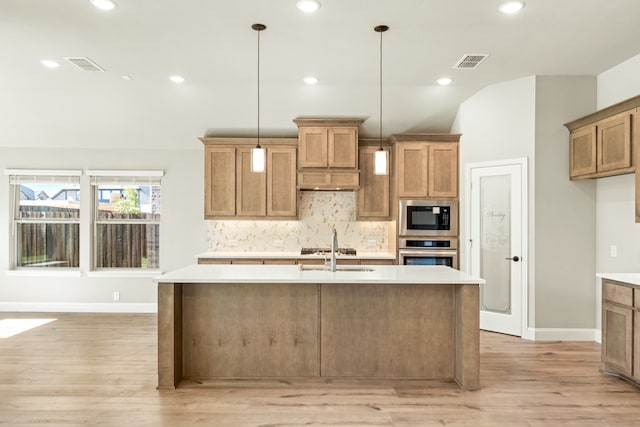 kitchen with a kitchen island with sink, light hardwood / wood-style flooring, backsplash, pendant lighting, and appliances with stainless steel finishes