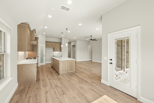 kitchen featuring pendant lighting, light hardwood / wood-style floors, sink, and an island with sink