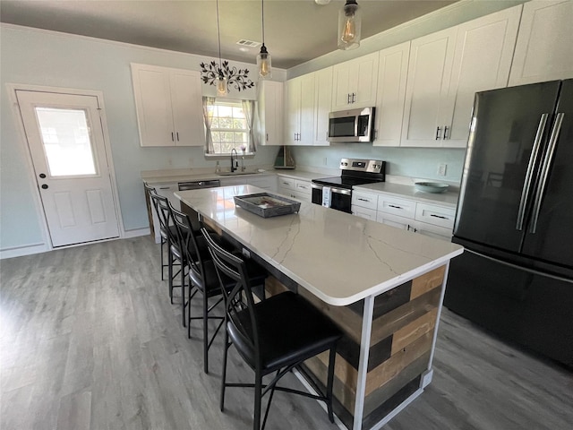 kitchen featuring pendant lighting, appliances with stainless steel finishes, a kitchen island, a kitchen bar, and white cabinetry