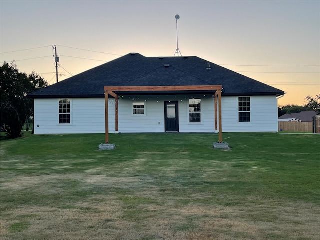 back house at dusk featuring a lawn