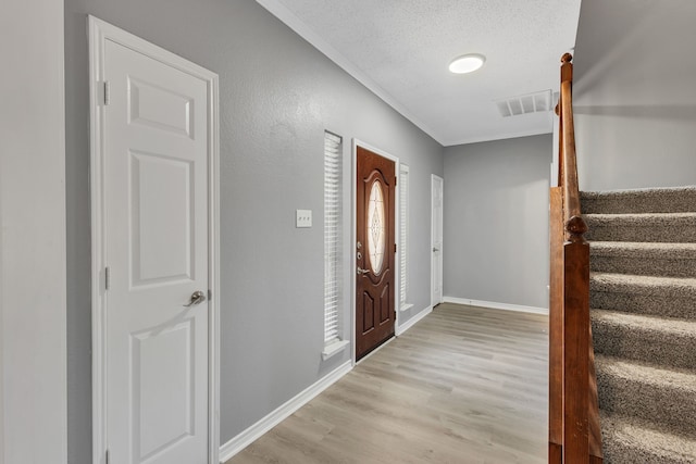 entrance foyer with a textured ceiling, light hardwood / wood-style flooring, and ornamental molding