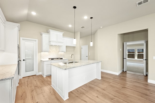 kitchen featuring a center island with sink, sink, white cabinets, light stone counters, and light hardwood / wood-style floors