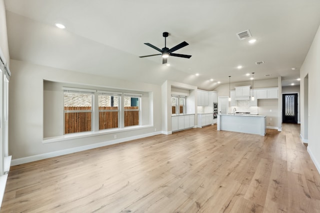 unfurnished living room with light hardwood / wood-style floors, vaulted ceiling, and ceiling fan