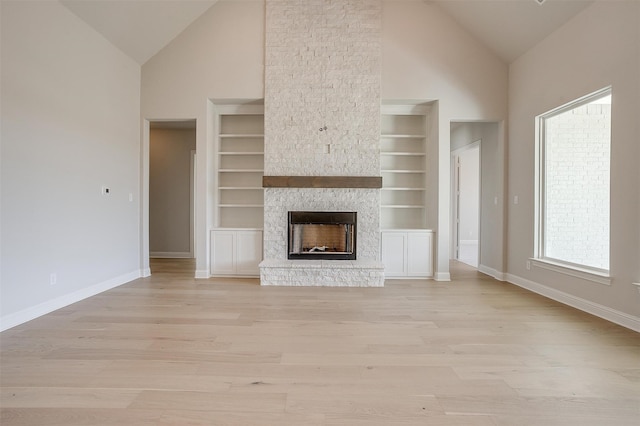 unfurnished living room featuring light hardwood / wood-style flooring, a stone fireplace, built in shelves, and high vaulted ceiling