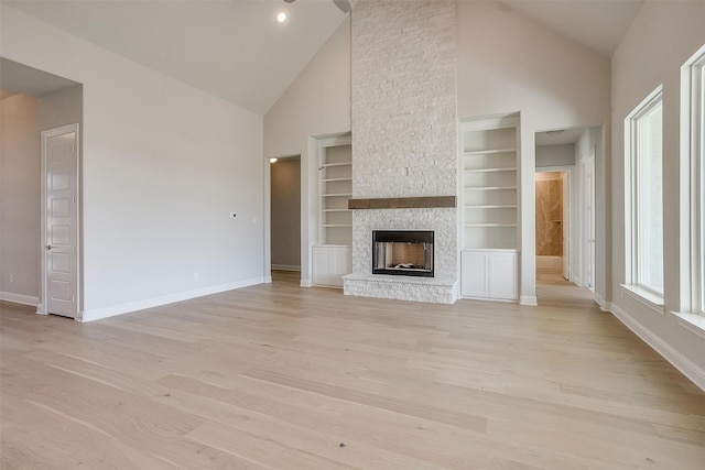 unfurnished living room featuring light hardwood / wood-style floors, high vaulted ceiling, built in shelves, and a stone fireplace