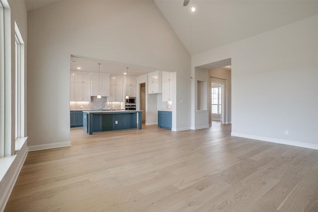 unfurnished living room featuring light hardwood / wood-style floors, high vaulted ceiling, and sink