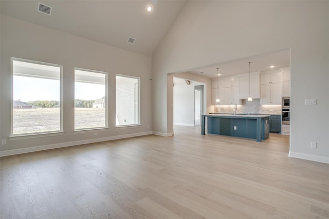 unfurnished living room featuring high vaulted ceiling, sink, and light wood-type flooring