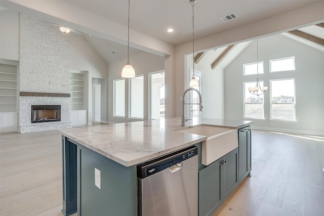 kitchen with a stone fireplace, beamed ceiling, an island with sink, hanging light fixtures, and stainless steel dishwasher