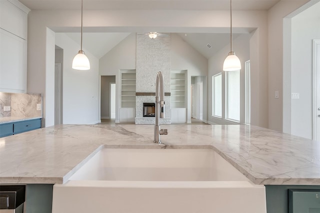 kitchen with a stone fireplace, tasteful backsplash, decorative light fixtures, and sink