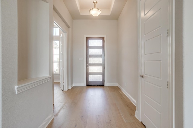 foyer entrance with light wood-type flooring and a raised ceiling