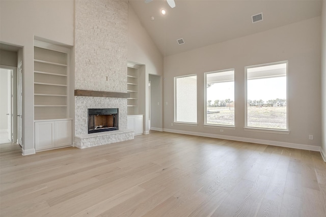 unfurnished living room featuring a stone fireplace, built in features, ceiling fan, light hardwood / wood-style floors, and high vaulted ceiling