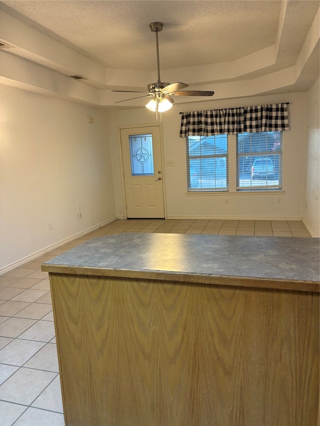 tiled spare room with a tray ceiling, a healthy amount of sunlight, a textured ceiling, and ceiling fan