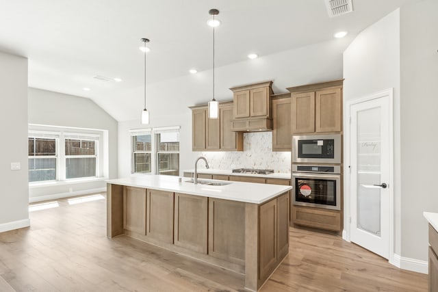 kitchen with light wood-type flooring, appliances with stainless steel finishes, plenty of natural light, and a center island with sink