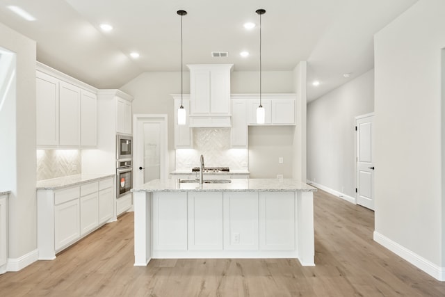 kitchen with white cabinets, a kitchen island with sink, stainless steel appliances, and light stone counters